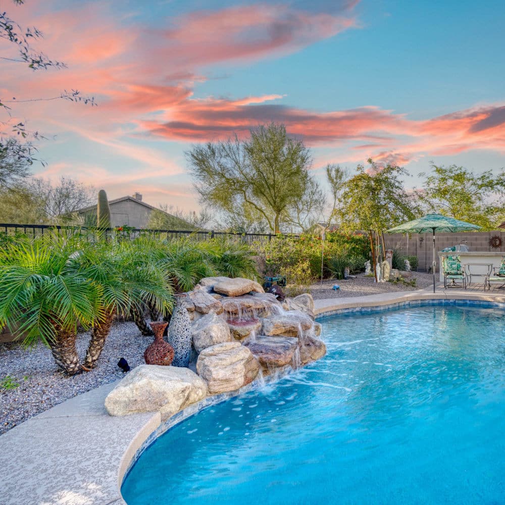 Luxury home pool at sunset with a waterfall